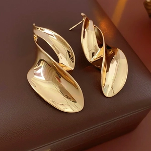 Macro detail of golden irregular leaf earrings on textured dark brown leather surface