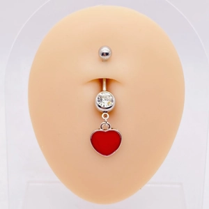 Macro shot of silver navel ring with a sparkling clear gem and red heart pendant