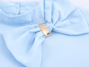 Detail shot of a light blue blouse neckline with a bow and gold metal ring accent