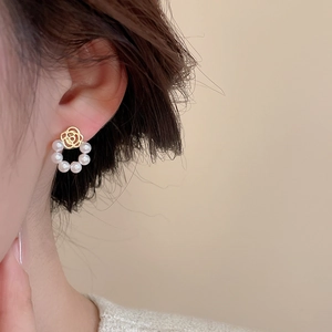 Close-up of golden hollow flower earrings with a white pearl circle worn by a model