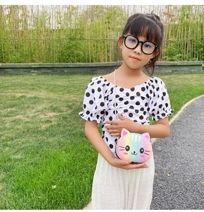Outdoor shot of a girl wearing a rainbow cat-shaped crossbody bag with a polka dot top