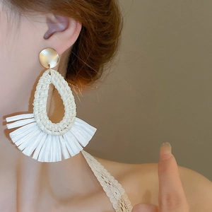 Détail macro de boucles d'oreilles bohèmes en raphia tressé blanc avec pompon éventail