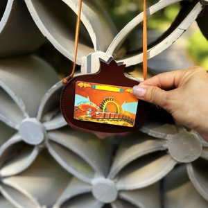Close-up of brown leather pomegranate card holder with orange lanyard on stone background