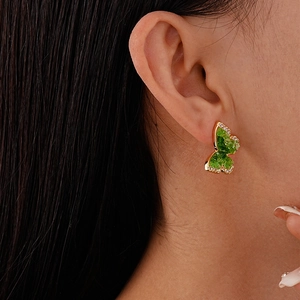 Close-up of green crystal butterfly stud earrings with gold plating on female ear