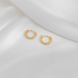 Detail of gold geometric huggie earrings with textured relief on white silk background