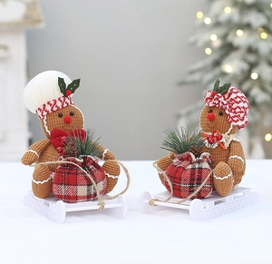 Detailed view of gingerbread plush dolls sitting on white sleds with gift bags