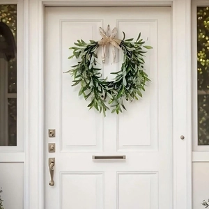 Olive leaf wreath with a beige bow hanging on a white wooden door for home decoration
