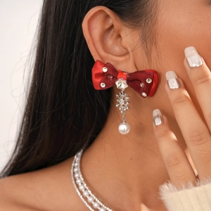 Detail of red bow earring with rhinestones, silver snowflake, and pearl on model