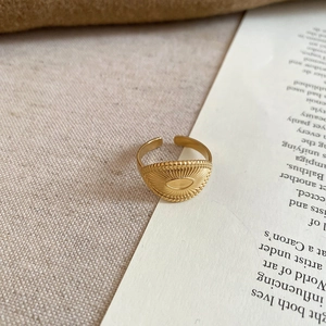 Detail of gold sunburst eye engraving on stainless steel ring over aesthetic background