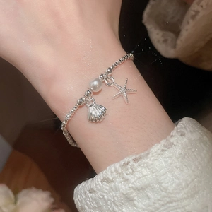 Dettaglio del bracciale a sfere argentate con ciondoli a forma di perla, stella marina e conchiglia