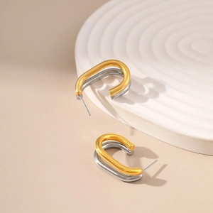 Detail of two-tone gold and silver C-shaped twisted earrings on a white wavy tray