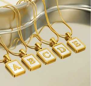 Detailed view of five gold snake chains with square mother of pearl letter pendants A to E
