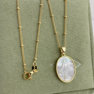 Golden Virgin Mary necklace with oval shell pendant and beaded chain on green jewelry box