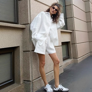 Detail of white oversized linen shirt and shorts set on a model against a stone wall