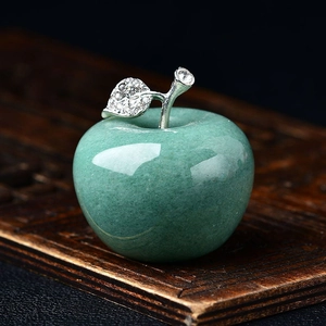 Macro shot of green jade apple figurine with sparkling silver leaf detail on wood