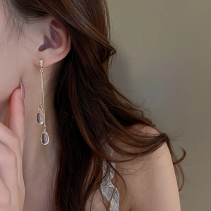 Close-up of elegant gold tassel earrings with clear teardrop pendants worn by model