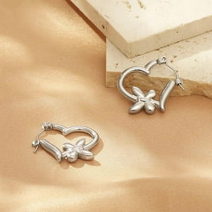 Detailed close-up of heart-shaped steel earrings with a four-petal flower design