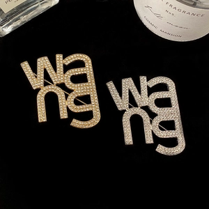 Minimalist gold and silver WANG letter brooches with crystals on black velvet
