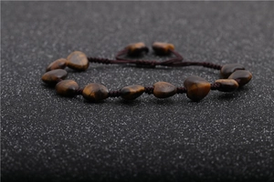 Detailed view of heart-shaped tiger eye stone beads on a brown braided adjustable bracelet