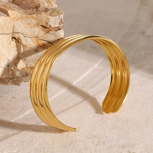 Minimalist gold stainless steel open bangle with layered groove design on stone background