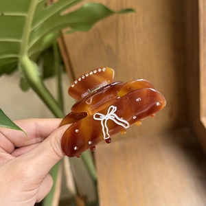 Detail of amber tortoiseshell hair claw with white bow pattern and sparkling rhinestones