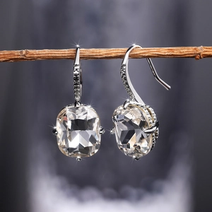 Macro shot of silver cushion-cut zircon earrings hanging on a natural wooden branch