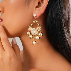 Close-up of golden floral stud earrings with rhinestone ball pendant on model