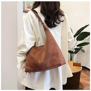 Close-up of large brown suede hobo tote bag worn by a model in a warm room