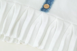 Détail d'une jupe en maille plissée avec bordure en denim bleu et bouton doré en relief
