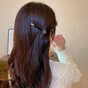 Detail of a black velvet camellia hair clip with gold hollow petals on brown hair
