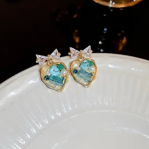 Detail of heart-shaped earring featuring bow design and turquoise inlay on ceramic dish