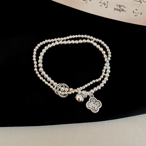 Macro detail of silver double-layer beaded bracelet with bell and peanut charm pendant