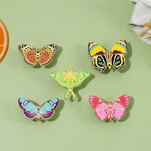 Detail of five colorful butterfly enamel pins with gold trim on a soft green background