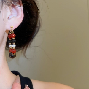 Close-up of vintage beaded drop earrings with pearl, black stone and red beads on model