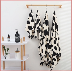Detailed view of soft coral fleece cow print towel set hanging in a warm bathroom setting