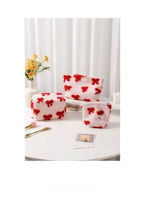 Detailed macro view of pink plush cosmetic bags with embroidered red bows and metal zipper