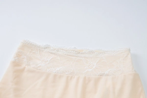 Close-up of champagne silk fabric with intricate floral lace trim and high-waist band