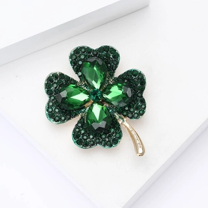 Detail of green rhinestone four-leaf clover brooch with gold-tone stem on white background
