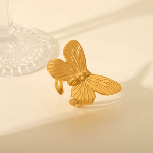 Close-up of a golden butterfly ring with adjustable open band on a warm beige background
