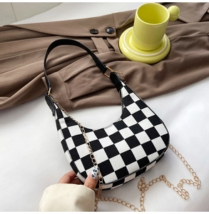 Detail of checkered hobo bag with black leather strap and gold chain on fabric