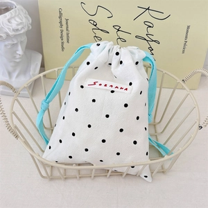 Close-up of white cotton drawstring pouch with black polka dots in a white metal basket