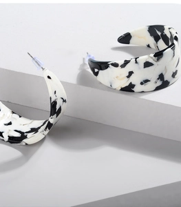 Macro shot of black and white acetate C-shaped earrings on minimalist white steps