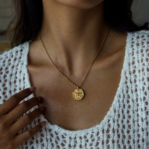 Close-up of golden stainless steel coin pendant necklace with embossed design on model