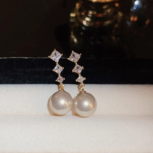 Detailed macro view of gold-plated drop earrings featuring clear crystals and white pearls