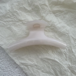 Detailed view of a creamy white translucent hair claw clip on a textured beige paper background