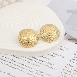 Detailed view of golden spiral woven stud earrings on a white rippled display plate