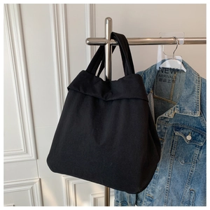 Minimalist black oversized fabric tote bag displayed on a rack with a denim jacket