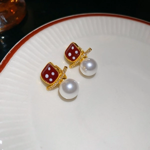 Detailed macro shot of 18K gold plated dice and pearl earrings on a porcelain plate