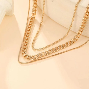 Detailed view of layered gold cuban and snake chain necklaces on beige display stand