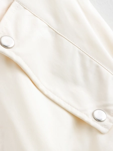 Detaillierte Makroansicht von cremefarbenem Twill-Stoff und silbernen Metallknöpfen der Weste